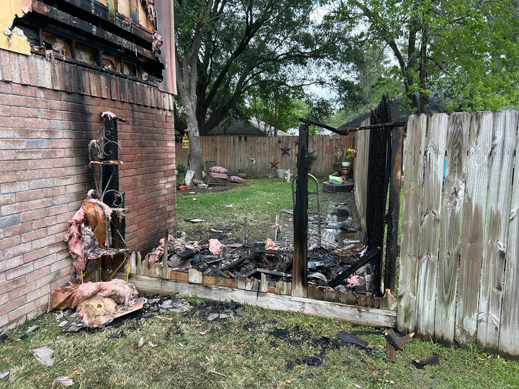 Backyard fire damage in Montgomery, TX showing burned fence, charred brick wall, and destroyed furniture.